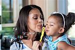 Mid adult mother and young girl blowing bubbles, close up