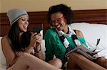 Young women sitting on bed using mobile phone, laughing