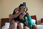Young women sitting on bed taking self portrait with mobile phone