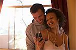 Young couple listening to mp3 player in hotel room, smiling