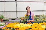 Mid adult woman carrying flowers in garden centre, smiling