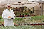 Senior man holding clipboard in garden centre, portrait