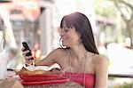 Young woman holding mobile phone in outdoor cafe, smiling