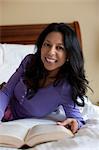 Mature woman lying on bed holding book, portrait