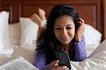 Mature woman lying on bed looking at mobile phone, smiling
