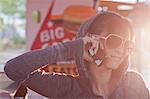Young woman in sunglasses using mobile phone in sunlit diner