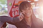 Young woman using mobile phone in sunlit diner, smiling