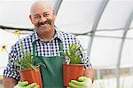 Mature man holding plant pots in garden centre, portrait