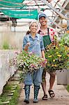 Young woman and mature man walking with hanging baskets in garden centre