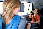 Mother watching boy drink from bottle in back seat of car