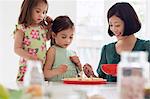 Mother and two daughters spooning topping onto tarts