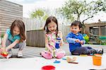 Three young children painting and drawing in garden