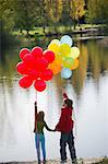 Brother and sister with bunches of balloons in park