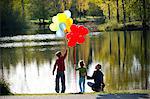 Mother and children in front of lake with bunches of balloons