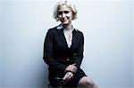 Studio portrait of blond businesswoman sitting on stool