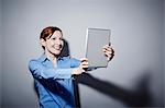 Studio portrait of young woman holding up digital tablet