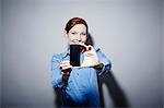 Studio portrait of young woman holding up camera phone