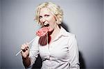 Studio portrait of mature woman biting into red lollipop