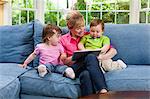 Grandmother and grandchildren on sofa looking at digital tablet