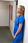 Nurse in blue scrubs in leaning against wall in hospital corridor