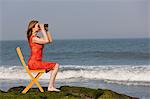 Mature woman sitting on chair on beach with binoculars