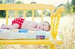 Newborn baby girl lying on yellow bench in field