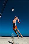 Male beach volleyball player jumping mid air to hit ball