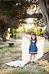 Portrait of girl holding sheet with arms out under tree