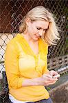 Woman using mobile phone against chain link fence