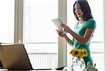 Woman holding digital tablet looking at laptop