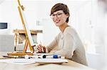 Portrait of smiling woman painting at easel on table