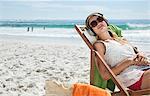 Serene woman listening to headphones in lounge chair on beach