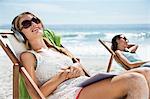 Serene woman listening to headphones in lounge chair on beach