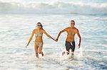 Portrait of happy couple holding hands and running in ocean