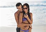 Happy couple hugging and looking at cell phone on beach