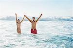 Portrait of enthusiastic couple holding hands with arms raised in ocean