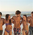 Happy friends in bikinis and swim trunks hugging on beach