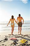 Couple holding hands and walking toward ocean on beach