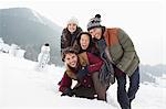 Portrait of happy friends in snowy field with snowman