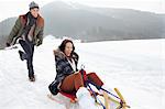 Enthusiastic couple sledding in snowy field