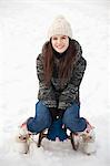 Portrait of smiling woman sitting on sled in snow