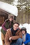 Portrait of smiling father and sons in snow outside cabin