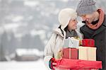 Happy couple carrying Christmas gifts in snow