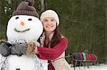 Happy woman hugging snowman in woods