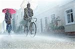 Couple with umbrellas riding bicycles in rain