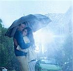 Happy couple hugging under umbrella in rain