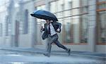 Businessman with umbrella running across rainy street