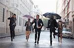 Business people with umbrellas running in rainy street