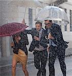 Happy business people with umbrellas running in rainy street