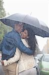 Portrait of happy couple hugging under umbrella in rain